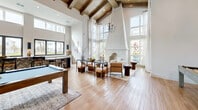Located at 1700 Ranch Rd in Nokomis, Florida, this single-story community clubhouse offers a generously sized and thoughtfully designed amenity space. The reception area greets visitors with soaring double-height windows, an abundance of natural light, warm neutral tones, and a striking drum pendant light, creating a polished yet welcoming atmosphere. A dedicated conference room, accessible through sleek black-framed glass doors, provides a quiet workspace furnished with a wooden desk, curated artwork, and soft natural light from exterior windows. The social lounge is a standout feature, boasting dramatic vaulted ceilings with exposed wood beams, a chandelier, a pool table set beneath elegant archways, and a bar area with seating — ideal for gatherings and entertainment. A café-style lounge area offers built-in banquette seating, round wooden tables, and gold-accented pendant lighting, flowing seamlessly into the broader common areas through arched doorways. The fitness center is well-appointed across two areas, featuring a full suite of strength-training machines, free weights, rowing equipment, floor-to-ceiling mirrors, mounted televisions, and exposed beam ceilings with ceiling fans. Throughout the space, neutral palettes, textured carpeting, hardwood-style flooring, and carefully selected artwork create a cohesive, upscale Florida aesthetic.