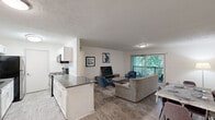 This thoughtfully designed 3-bedroom, 2-bathroom residence offers comfortable single-floor living with a practical and open layout. The combined kitchen and living room serves as the heart of the home, featuring light hardwood-style flooring that flows throughout the main living areas. The kitchen is outfitted with white shaker cabinetry, a classic subway tile backsplash, dark gray countertops, and stainless steel appliances including a refrigerator, range, microwave, and dishwasher. A peninsula provides additional counter space and a natural transition into the open dining and living area. The living room is bright and welcoming, anchored by a sliding glass door that opens to a private balcony overlooking lush, mature greenery. The three bedrooms feature plush carpeting and natural light from well-positioned windows. The primary bedroom offers a comfortable footprint, while a secondary bedroom features dual closets for generous storage. Both bathrooms are fitted with full soaking tub and shower combinations accented by clean white tile surround and brushed nickel fixtures. A hallway and dedicated closet round out the floor plan, ensuring ample storage throughout this well-organized and move-in ready residence.