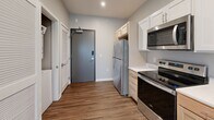 This single-floor unit is designed with a clean, modern aesthetic and an efficient, open layout. The kitchen and living area flow seamlessly together, creating a spacious, connected environment ideal for both daily living and entertaining. The kitchen is equipped with stainless steel appliances, including a refrigerator, electric range, built-in microwave, and dishwasher. Cabinetry combines white upper cabinets with light wood lower cabinets, complemented by white countertops and a single-basin sink. A louvered closet near the entry provides additional storage, and a dedicated laundry area is also present.

The open living area benefits from rich, wood-style flooring that extends throughout the unit, offering a warm and cohesive visual appeal. A large sliding glass door with vertical blinds fills the living space with natural light and provides access to the exterior. A secondary window further brightens the room.

The bedroom features vaulted ceilings, a ceiling fan with integrated lighting, a window with horizontal blinds, and direct access to a private bathroom. Neutral gray walls throughout maintain a calm, contemporary atmosphere. Recessed lighting adds a polished touch to the overall design.