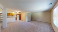 This single-floor residence offers a functional and straightforward layout designed for comfortable everyday living. The open main living area is finished with neutral-toned wall-to-wall carpeting, creating a warm and cohesive feel throughout. A ceiling fan light fixture provides both illumination and airflow, while a set of double closet doors along one wall offers convenient built-in storage. The adjoining kitchen is well-appointed with warm-toned wooden cabinetry extending to the upper walls, granite-style countertops, and white appliances including a gas range, over-the-range microwave, dishwasher, and refrigerator. Light tile flooring completes the kitchen's clean and practical aesthetic. The bedroom is a generously sized, carpeted room featuring a large window that invites natural light and offers views of the surrounding greenery. An open closet with a hanging rod provides ample storage. A second carpeted room with its own window and a full-length door adds flexibility as a bedroom, office, or flex space. The bathroom features a full tub-shower combination with white tile surround, chrome fixtures, and a clean, classic finish. Throughout the unit, neutral tones and simple finishes create a bright, move-in ready environment.