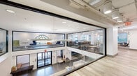 Located at 8204 Baltimore Ave in College Park, Maryland, this thoughtfully designed commercial space occupies a single expansive floor, offering a versatile and contemporary environment suited for collaboration and productivity. The layout is characterized by an open-plan design that flows seamlessly between distinct functional zones, all tied together by light wood-look flooring, crisp white walls, and exposed ceiling infrastructure that lends an industrial-modern aesthetic.

A dramatic floor-to-ceiling glass wall system defines the main entry area, providing transparency and visual connectivity throughout. A striking vertical wood slat partition with integrated greenery adds warmth and biophilic design elements to one corridor zone. Signature arched windows, echoing classic architectural details, fill seating nooks with abundant natural light and serve as focal points throughout.

Collaborative lounge areas feature plush sofas, colorful high-back accent chairs, and nature-inspired decorative dividers. A dedicated dining and meeting area offers banquette seating, communal tables, and vibrant artwork panels, ideal for group gatherings or focused work. Smaller enclosed rooms with glass frontage provide private meeting spaces. The overall ambiance is bright, welcoming, and professionally curated, balancing openness with purposeful areas for both individual and collective use.