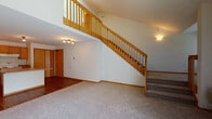 This two-story space is thoughtfully designed to maximize openness and functionality across both levels. The main level features a seamless transition between the living area and kitchen, with durable hardwood flooring running throughout the kitchen and entry zones, while plush carpet defines the living space. The kitchen is well-equipped with warm-toned oak cabinetry, white appliances including a refrigerator, electric range, and dishwasher, and a central island that provides additional counter and storage space. The open layout allows clear sightlines between the kitchen and living area, enhancing the sense of spaciousness.

A striking wood-railed staircase connects the main level to the upper floor, where an open railing overlooks the living area below, adding visual depth and an airy feel. The upper level features carpeted bedrooms, including a generously sized primary room with a ceiling fan and vaulted ceiling that draws the eye upward. Natural light filters in through a sliding glass door on the main level and windows upstairs. The upper-level hallway provides access to a bathroom with a wide vanity, oak cabinetry, and ample storage, as well as additional rooms with wood-paneled closet doors. A skylight brightens the upper hallway, completing the space's warm, welcoming atmosphere.