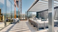 Located in the heart of downtown Salt Lake City at 209 E 300 S, this expansive rooftop terrace offers a sophisticated outdoor retreat with stunning panoramic views of the Wasatch Mountains and the surrounding urban skyline. The terrace is thoughtfully designed with distinct zones to accommodate a variety of uses and group sizes.

Overhead pergola structures provide partial shade across multiple seating areas, which are furnished with plush, neutral-toned sectional sofas, lounge chairs, and dining tables suited for both casual gatherings and structured social events. Floor-to-ceiling glass curtain walls enclose an adjacent interior lounge, seamlessly connecting indoor and outdoor spaces while allowing abundant natural light to flow throughout.

A generous sun deck lined with rows of chaise lounges invites relaxation under open skies, flanked by raised planter beds filled with ornamental grasses, flowering plants, and seasonal greenery that add texture and a natural aesthetic to the modern hardscape. Large-format tile paving extends throughout the terrace, contributing to the clean, contemporary character of the space.

The terrace benefits from unobstructed sightlines in multiple directions, framing iconic views of Salt Lake City's downtown towers alongside the rugged mountain backdrop—making it a standout amenity space with a distinctive sense of place and elevation.