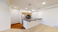 Located at 4250 E Poleline Ave in Post Falls, Idaho, this single-floor unit offers a well-designed open-concept layout that integrates the kitchen and living areas seamlessly. The kitchen is a standout feature, equipped with stainless steel appliances including a refrigerator and range, warm-toned wood cabinetry, a dark tile backsplash, and a spacious peninsula with a built-in sink and dark countertop. Pendant lighting fixtures hang above the peninsula, complementing the recessed lighting throughout. The kitchen transitions into the living area, where rich hardwood-style flooring gives way to neutral wall-to-wall carpeting. Baseboard heating is present throughout, and a wall-mounted HVAC unit provides additional climate control options. The living space benefits from natural light through large windows and a glass exterior door that opens to an outdoor area with green views. Bedrooms are carpeted and feature closets with bifold doors, offering practical storage. The bathroom includes a full tub/shower combination, a wood-vanity with integrated sink, light tile flooring, and a lighted mirror. Clean, neutral finishes and a functional floor plan define the overall character of this space.