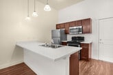Unit 302 at 16815 Redmond Way is a well-appointed 820-square-foot, two-bedroom, one-bathroom apartment in Redmond, WA. The open-concept kitchen and living area serves as the heart of the unit, featuring a peninsula with a quartz countertop and integrated sink, two-tone cabinetry with warm wood lower cabinets and gray upper cabinets, a tile backsplash, stainless steel appliances including a refrigerator, range, microwave, and dishwasher, and pendant lighting. Hardwood-style flooring runs throughout the entire unit, lending a cohesive and contemporary feel. The primary bedroom spans 140 square feet and includes a ceiling fan, a large window with views of the surrounding community, and direct access to a dedicated closet with built-in shelving rods. The second bedroom is equally bright, featuring its own large window and wall-mounted climate control. The bathroom is finished with a soaking tub and shower combination framed by floor-to-ceiling white tile, wood-toned vanity cabinetry, quartz countertops, an illuminated mirror, and matte black fixtures. A dedicated laundry area with a stacked washer and dryer unit rounds out this functional and modern apartment.