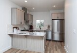 Located at 6328 W State St in Boise, Idaho, this two-story property showcases a clean, contemporary design throughout. The main level features an expansive open-plan living and kitchen area with warm hardwood flooring and recessed lighting that creates a bright, welcoming atmosphere. The kitchen is thoughtfully appointed with light wood cabinetry, white quartz countertops, a subway tile backsplash, stainless steel appliances including a gas range and refrigerator, and a matte black faucet over an undermount sink. A peninsula provides additional counter space and casual seating. A convenient full bathroom is also accessible on the main level. Upstairs, carpeted bedrooms offer a comfortable retreat, with windows framing views of the surrounding landscape, including open green spaces and mature trees. The bathrooms are finished with neutral tile flooring, wood-toned vanities with white quartz tops, and matte black hardware — one featuring a glass-enclosed walk-in shower with white subway tile, and the other a shower-tub combo. A carpeted staircase with a clean white handrail connects the two levels. Throughout the property, a consistent palette of whites, natural wood tones, and matte black accents lends a cohesive, modern aesthetic.