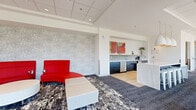 This well-appointed social room at 2060 Quingate Place in Halifax, Nova Scotia, offers a thoughtfully designed communal space spanning a generous single floor. The open-concept layout seamlessly connects a fully equipped kitchen, a relaxed lounge area, and dedicated workspaces, making it a versatile hub for both social gatherings and productive work sessions.

The kitchen is a standout feature, anchored by a striking marble-topped island with pendant lighting overhead — elegant egg-shaped fixtures with warm gold interiors. Dark navy cabinetry lines the walls, complemented by light tile backsplash, stainless steel appliances, and a clean white countertop shelf. The adjacent lounge area features bold red seating set against a textured accent wall, adding a vibrant pop of color to the bright, neutral palette.

Floor-to-ceiling windows along one wall flood the space with natural light and offer open views of the surrounding greenery and streetscape. A long communal table positioned against these windows provides an ideal setting for collaborative work or casual gatherings. A dedicated meeting room features a marble conference table, acoustic wall panels, bold red pendant lights, and a wall-mounted display screen. The office area offers a focused, clean workspace with functional desks and task chairs. Patterned area rugs and light hardwood flooring complete the polished, contemporary aesthetic throughout.