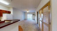Located at 2130 South Ave in La Crosse, Wisconsin, this single-floor unit offers a practical and comfortable layout suited for everyday living. The living area is generously sized, finished with plush wall-to-wall carpeting and neutral-toned walls that create a clean, open atmosphere. A sliding glass door allows natural light to pour in and provides outdoor access. Baseboard heating runs throughout the unit, ensuring consistent warmth. The kitchen is well-appointed with rich dark wood cabinetry, dark countertops, hardwood-style flooring, a white electric range, and a full-size refrigerator. A curved breakfast bar peninsula separates the kitchen from the living space, adding both function and visual interest. The hallway connects the main living areas to the bedroom, which features soft carpeting, a window for natural light, and access to a dedicated walk-in closet with built-in shelving — offering ample storage. The bathroom includes a wide vanity with a large mirror, wood cabinetry below, and additional mirrored medicine cabinets. The unit's straightforward, efficient design makes it an accessible and functional space throughout.