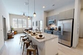 Located at 4500 University Dr in Fairfax, VA, this well-appointed 5-bedroom, 4-bathroom unit offers a thoughtfully designed single-floor layout. The open-concept kitchen and living area serves as the heart of the space, anchored by a large granite-topped island with seating for multiple guests. The kitchen is outfitted with stainless steel appliances — including a French door refrigerator, electric range, over-the-range microwave, and dishwasher — complemented by sleek gray cabinetry, white subway tile backsplash, and pendant lighting. Light hardwood flooring flows throughout, enhancing the bright, airy feel. The living room features tall ceilings, a ceiling fan, and large windows that fill the space with natural light and offer views of the surrounding area. Each of the five bedrooms is a comfortable private retreat, with the primary bedroom offering generous proportions and a dedicated closet with built-in shelving. The four bathrooms are clean and modern, featuring tiled shower-tub combinations, neutral finishes, and granite vanity surfaces. A hallway connects the bedroom wing to the main living areas, and a dedicated closet provides additional storage. The overall aesthetic is contemporary and cohesive, with a neutral color palette throughout.