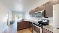 Located at 16790 Chandler Rd in East Lansing, MI, this well-designed one-bedroom, one-bathroom unit offers a thoughtfully utilized single-floor layout. The open-concept kitchen and living area serves as the heart of the space, featuring warm wood-tone cabinetry, granite countertops, a subway tile backsplash, and a full suite of stainless steel appliances including a refrigerator, range, microwave, and dishwasher. A kitchen island with seating provides a casual dining option and adds to the functional flow of the space. The living area is bathed in natural light through a full-width sliding glass door fitted with vertical blinds, offering pleasant outdoor views and a bright, airy atmosphere. Wood-look flooring runs throughout the main living areas, adding warmth and continuity. The bedroom is a comfortable, well-proportioned room with plush carpet flooring and a window that brings in additional natural light. The bathroom is finished with a rich dark wood vanity, granite countertop, a large mirror, and wood-look flooring, complemented by accessibility-friendly grab bars. Clean white walls and recessed lighting throughout give the unit a crisp, modern feel.