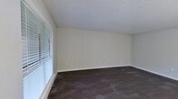 This single-story, one-bedroom, one-bathroom unit offers an efficient and thoughtfully arranged layout across a compact footprint. Dark hardwood-style flooring runs throughout the main living areas and bedroom, providing a consistent and grounded aesthetic against the neutral gray-toned walls. Textured ceilings are present throughout the unit.

The combined kitchen and living room area forms the heart of the space. The living room receives natural light through a large window fitted with horizontal blinds and a sliding glass door dressed with vertical blinds, accompanied by a ceiling fan with light fixture. The galley-style kitchen is well-appointed with dark espresso cabinetry, granite-style countertops, a double stainless steel sink, black appliances including a refrigerator and electric range, a stainless steel microwave, and a mosaic tile backsplash. Pendant lighting adds a polished touch above the counter area.

The bedroom is a comfortable size, featuring two windows that bring in natural light. It is served by a dedicated walk-in closet with built-in shelving and hanging rods on multiple walls, offering generous storage. The bathroom continues the dark cabinetry theme, with a granite-style countertop vanity and tile-accented walls, maintaining a cohesive design throughout the unit.