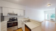 Located at 7550 N Lombard St in Portland's St. Johns neighborhood, Unit 303 is a single-floor residence designed with a clean, modern aesthetic. Warm hardwood-style flooring runs throughout the living areas and bedroom, creating a cohesive and inviting atmosphere. The open-concept layout connects the living area to the kitchen, which features white shaker cabinetry, open shelving, quartz countertops, a subway tile backsplash, stainless steel appliances — including a gas range and dishwasher — and a peninsula with a built-in sink that doubles as a casual dining or prep space. The living area is bright and open, with a door that leads to a view of surrounding greenery, filling the space with natural light. The bedroom is a comfortable, well-proportioned room with a window overlooking mature trees, offering a serene outdoor view. A closet with louvered bi-fold doors provides ample storage. The bathroom includes a full soaking tub and shower combination with clean white surrounds and chrome fixtures. A stacked washer and dryer unit is conveniently housed within the unit, adding to the overall practicality of the space. The layout is efficient and functional, making effective use of every area.