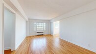 Located at 2680 N Moreland Blvd in Cleveland's Shaker Square neighborhood, this well-maintained single-floor unit offers a clean, light-filled interior defined by warm hardwood flooring and crisp white walls throughout. The spacious living area features wide-plank hardwood floors, a large multi-pane window that draws in generous natural light, and a baseboard heating unit, creating a bright and comfortable gathering space. A connecting hallway with recessed lighting leads seamlessly to the private rooms. The bedrooms are distinguished by classic herringbone-patterned hardwood floors, ceiling fans, and windows that allow ample sunlight to filter in; one bedroom includes a built-in closet with shelving. The kitchen is equipped with stainless steel appliances including an electric range, granite countertops, gray cabinetry, and white tile flooring, offering a functional and modern cooking space. A bathroom with classic fixtures is also present. Throughout the unit, the combination of traditional herringbone and straight-lay hardwood floors, white panel doors with black hardware, and an abundance of natural light from multiple windows creates a cohesive, timeless aesthetic that balances classic character with modern updates.