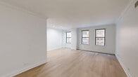 Located at 200 East Chestnut Street in Chicago's prestigious Gold Coast neighborhood, this well-appointed one-bedroom, two-bathroom residence offers a clean, modern aesthetic throughout. Light-toned hardwood flooring flows seamlessly across the living room, hallway, and spacious primary bedroom, creating a warm and cohesive interior.

The living room is bright and open, with recessed lighting and views into the adjacent kitchen. The kitchen features a galley-style layout with rich dark cabinetry, white countertops, stainless steel appliances including a refrigerator, electric range, and built-in microwave, and tile flooring — offering efficient use of space with a polished finish.

The generously sized primary bedroom includes multiple built-in closets with paneled doors and a window overlooking lush greenery, filling the room with natural light. A second window in the living area further enhances the bright, airy atmosphere.

The two bathrooms offer distinct designs: one features a dark wood vanity with a white countertop, subway tile surround, and tile flooring, while the second presents an all-white palette with a pedestal sink and subway tile wainscoting. Both are clean and functional. A hallway connects all rooms, completing this efficiently designed urban residence.