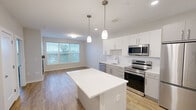 Located at 83 Pleasant Valley St in Methuen, Massachusetts, this well-designed one-bedroom, one-bathroom unit offers a thoughtful layout with modern finishes throughout. The kitchen serves as a central highlight, featuring sleek white cabinetry extending to the ceiling, a classic subway tile backsplash, quartz countertops, a kitchen island with pendant lighting, and a full suite of stainless steel appliances including a dishwasher, range, microwave, and refrigerator. Light hardwood-style flooring runs throughout the main living areas, enhancing the bright and open feel of the space. The living area flows naturally from the kitchen, creating an inviting, functional environment. The bedroom offers plush carpeting and a window with views of the surrounding greenery, allowing natural light to fill the room. A dedicated walk-in closet with rod storage provides ample organizational space. The bathroom is finished with a clean, minimalist aesthetic, featuring a wide vanity with a quartz countertop, an under-mount sink, warm cabinetry, a large mirror with overhead lighting, and polished chrome fixtures. Recessed lighting and neutral tones throughout lend the unit a cohesive, contemporary character.