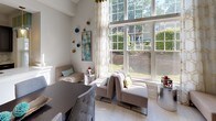 This single-floor residence is designed around an open-concept floor plan that seamlessly connects the kitchen, dining, and living areas into one cohesive, light-filled space. The kitchen is outfitted with dark cabinetry contrasted by light granite countertops, a large central island with an undermount sink, stainless steel appliances, and decorative pendant lighting with an amber glass finish. A tile backsplash and light porcelain tile flooring carry throughout, adding a clean, contemporary feel.

The adjacent living and dining areas benefit from dramatically tall ceilings and an expansive floor-to-ceiling window wall that floods the interior with natural light and frames views of lush greenery outside. The living room is anchored by a sleek fireplace set against a chevron-patterned accent wall, complemented by a built-in shelving unit that offers both display and storage functionality. Wall sconces and tasteful décor accents add warmth to the space. The overall ambiance is modern yet inviting, with a neutral palette punctuated by teal and gold tones that lend a polished, curated character throughout the home.