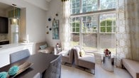 This single-floor residence is designed around an open-concept floor plan that seamlessly connects the kitchen, dining, and living areas into one cohesive, light-filled space. The kitchen is outfitted with dark cabinetry contrasted by light granite countertops, a large central island with an undermount sink, stainless steel appliances, and decorative pendant lighting with an amber glass finish. A tile backsplash and light porcelain tile flooring carry throughout, adding a clean, contemporary feel.

The adjacent living and dining areas benefit from dramatically tall ceilings and an expansive floor-to-ceiling window wall that floods the interior with natural light and frames views of lush greenery outside. The living room is anchored by a sleek fireplace set against a chevron-patterned accent wall, complemented by a built-in shelving unit that offers both display and storage functionality. Wall sconces and tasteful décor accents add warmth to the space. The overall ambiance is modern yet inviting, with a neutral palette punctuated by teal and gold tones that lend a polished, curated character throughout the home.