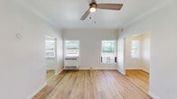This single-floor unit showcases a clean, contemporary design highlighted by light-toned hardwood flooring that runs seamlessly throughout the living areas and rooms. Crisp white walls and white baseboards create a bright, airy atmosphere, while multiple windows fitted with horizontal blinds invite natural light into every corner of the space.

The open living area is equipped with a ceiling fan and a wall-mounted air conditioning unit, ensuring year-round comfort. Multiple doorways connect the rooms in a functional layout, as seen in the 3D model overview, offering a smooth flow between spaces.

The galley-style kitchen is efficiently designed with slate-gray shaker-style cabinetry, light countertops, stainless steel appliances including a full-size refrigerator and gas range, and recessed lighting overhead. The kitchen's hardwood flooring ties cohesively into the rest of the unit.

The bathroom stands out as a refined retreat, featuring floor-to-ceiling large-format marble-look tile in warm gray tones with subtle veining. The deep soaking tub with a chrome fixture set adds a touch of elegance to the space.

Additional rooms offer versatility, each benefiting from natural light through blinds-covered windows. The entry door area provides a welcoming, clean entryway. Overall, this unit presents a well-maintained, move-in-ready space with modern finishes throughout.