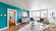 This thoughtfully designed one-bedroom, one-bathroom residence spans a single floor and offers a cohesive mid-century modern aesthetic throughout. The open living room serves as the heart of the unit, showcasing polished concrete floors, a striking teal accent wall, and expansive floor-to-ceiling sliding glass doors that flood the space with natural light and provide direct access to a private balcony with city skyline views. The balcony is outfitted with outdoor seating, making it an ideal extension of the living area.

The kitchen features warm wood cabinetry, granite countertops, stainless steel appliances including a full-size refrigerator, and light hardwood flooring. A dedicated hallway connects the living spaces to the private bedroom, which is appointed with plush carpeting, a bold terracotta-orange accent wall, a walk-in closet, and its own sliding glass door opening to the balcony — bringing in ample natural light and urban views.

The bathroom is clean and classic, featuring a full soaking tub and shower combination with white subway tile surround. Throughout the unit, the interplay of bold color choices, modern finishes, and abundant natural light creates a vibrant yet functional living environment well-suited to urban life.
