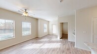 Located in Lago Vista, TX, this one-bedroom, one-bathroom residence offers a thoughtfully designed open-concept layout that maximizes every square foot. Light wood-look flooring runs throughout, lending a clean, cohesive aesthetic to the entire space. The combined living, dining, and kitchen area forms the heart of the home, bathed in natural light streaming through multiple windows fitted with blinds. A ceiling fan adds comfort to the living area, while the front entry door provides direct access to the outdoors. The kitchen features a granite-style countertop island with a double stainless steel sink, pendant lighting overhead, track lighting, and a full-size refrigerator — all designed for both function and style. The bedroom is generously proportioned, equipped with its own ceiling fan, dual windows, and direct access to a walk-in closet outfitted with multi-tier wire shelving, as well as an additional closet. The bathroom includes a granite-topped vanity with a large mirror, wood-toned tile shower surround, and wood-look flooring. A dedicated laundry area rounds out this well-appointed home, offering practical convenience within a bright, neutral interior.