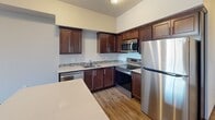 This 2-bedroom, 1-bathroom unit offers a thoughtfully designed single-floor layout that maximizes functionality within a compact footprint. The kitchen serves as a standout feature, finished with rich dark-brown cabinetry, light quartz countertops with a subtle mosaic tile backsplash, and a full suite of stainless steel appliances including a refrigerator, electric range, built-in microwave, and dishwasher. A central island provides additional prep and dining space, while light hardwood-style flooring and elevated ceilings lend an open, airy quality to the area.

The living space flows naturally from the kitchen, featuring the same hardwood-style flooring and neutral wall tones with dark wood baseboards throughout. The primary bedroom is a comfortable size and includes a walk-in closet with built-in hanging storage, while the second bedroom features plush carpeting and a large window offering outdoor views and abundant natural light.

The bathroom is generously proportioned, featuring a dark wood vanity, light wood-style flooring, and a convenient in-unit stacked washer and dryer. Consistent dark wood trim and door frames unify the overall aesthetic, creating a cohesive and well-finished interior throughout.
