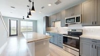 This two-story residence offers a well-designed layout divided equally across two levels, combining modern finishes with functional living spaces. The open-concept kitchen and living area anchors the main floor, showcasing grey shaker-style cabinetry, granite countertop surfaces, and a geometric white tile backsplash. A central island with matching granite provides additional workspace and casual dining potential, while sleek black pendant lights hang overhead. Stainless steel appliances, including a range, microwave, and dishwasher, complete the kitchen. Light-toned hardwood flooring runs throughout the main living areas, complementing the neutral grey wall palette and allowing natural light from the windows to brighten the space.

The bedroom is carpeted and comfortably sized, featuring a window with outdoor views, a dedicated closet, and a dark five-panel door that adds a contrasting design detail. Two bathrooms serve the residence; one features grey cabinetry, a granite-topped vanity, a framed mirror, and light hardwood flooring. A hallway and closet provide additional storage and circulation. The overall aesthetic is clean and contemporary, with a cohesive grey-and-neutral color scheme carried consistently throughout both floors.