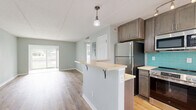 Located at 6742 Gulfport Blvd S in South Pasadena, FL, this thoughtfully updated single-story home offers four bedrooms and one bathroom across a compact, efficiently designed floor plan. The renovated kitchen is a standout feature, showcasing rich wood cabinetry, quartz countertops, stainless steel appliances including a range, microwave, and refrigerator, and a vibrant teal subway tile backsplash. A peninsula with a built-in wine cooler and bar seating adds both function and character, making the kitchen a central hub of the home. Light wood-tone luxury vinyl plank flooring runs throughout, lending warmth and continuity to every room. Each bedroom is finished in soft sage-green tones, with ceiling fans, ample natural light from slatted blinds, and closets with bifold doors for storage. The primary bedroom offers a generous footprint with outdoor views of lush greenery. The bathroom features a full soaking tub with bright white subway tile surround and a decorative mosaic accent border. A large window in the living area frames a tranquil waterfront view, filling the space with natural light and bringing the outdoors in. The exterior reveals a well-maintained green yard, completing this inviting Florida home.
