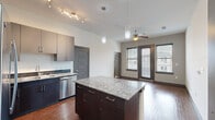 This well-appointed 2-bedroom, 3-bathroom single-floor unit in Denton, TX offers a thoughtfully designed layout with modern finishes throughout. The open-concept kitchen serves as the heart of the home, featuring a granite-topped center island with pendant lighting overhead, dark espresso cabinetry, a tile backsplash, and a full suite of stainless steel appliances including a refrigerator, range, microwave, and dishwasher. Rich hardwood-style flooring extends through the kitchen and living areas, creating a warm, cohesive aesthetic. The living area benefits from natural light through large windows with blinds and is equipped with a ceiling fan. Both bedrooms are carpeted and comfortably sized, with the primary bedroom offering its own dedicated closet space. The walk-in closet features wrap-around shelving and hanging rods for generous storage. The bathrooms are finished with granite-topped dark vanities and hardwood-style flooring, with one bath including a soaking tub surrounded by tile surround. Dark five-panel interior doors and consistent dark trim add a modern, unified design element throughout the space. A hallway connects the rooms efficiently, and two closets provide practical storage solutions for everyday living.