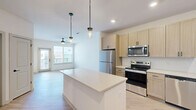 Located at 2220 Berryhill Road in Charlotte, NC, this well-designed one-bedroom, one-bathroom residence offers a thoughtfully organized single-floor layout. The open-concept living area seamlessly connects the kitchen, dining, and living spaces, creating an airy and functional atmosphere. The kitchen is equipped with stainless steel appliances—including a refrigerator, range, microwave, and dishwasher—complemented by light wood cabinetry, quartz-style countertops, a central island with pendant lighting, and light hardwood-style flooring that flows throughout the main areas. Natural light fills the living room through large windows and a glass door leading to a balcony, while a ceiling fan adds comfort overhead. The bedroom features plush carpeting, a ceiling fan, a natural light window, built-in shelving, and access to a spacious walk-in closet outfitted with wire shelving systems. The bathroom includes a full tub-shower combination with white tile surround and wood-look flooring. A dedicated laundry room houses a stacked washer and dryer unit, adding everyday convenience. Additional storage is provided by a utility room and a secondary closet, rounding out this efficiently designed residence.