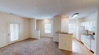 This single-story unit is designed with a practical, open layout that connects the living and dining areas to a galley-style kitchen. The living space features neutral-toned carpet and cream-colored walls, creating a clean, versatile backdrop. Natural light filters in through multiple windows, including a glass-paneled exterior door that adds additional brightness to the main living area.

The kitchen is well-equipped with white cabinetry, granite-look countertops, a stainless steel sink, and white appliances including a refrigerator, electric range with coil burners, and microwave. A peninsula-style breakfast bar separates the kitchen from the main living space, offering a casual dining option. Wood-look flooring in the kitchen adds a warm contrast to the carpeted areas. In-unit laundry connections are also visible within or adjacent to the kitchen space.

The bedrooms are carpeted and bright, each featuring windows with outdoor views and ample closet space, including walk-in storage in at least one room. The bathrooms feature wood-look flooring, chrome grab bars, and clean white fixtures. A vanity with granite-look countertops is present in one bathroom, adding a refined touch to the otherwise functional design. Overall, the unit presents a straightforward, comfortable living environment.