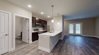Located at 4663 Crystal Ball Dr. in Hilliard, Ohio, this single-floor home offers a well-designed, open-concept layout with modern finishes throughout. The kitchen serves as a central highlight, featuring rich dark cabinetry, white countertops, stainless steel appliances including a range, microwave, and refrigerator, and a large center island with a built-in sink and pendant lighting overhead. The kitchen flows seamlessly into the living area, which is finished with wide-plank wood-style flooring and natural light streaming through a window. A set of French doors leads to the exterior, adding both light and accessibility. The living space is open and versatile, providing ample room for varied furniture arrangements. Bedrooms are carpeted for comfort and include windows that bring in natural light, with one bedroom offering access to a generously sized walk-in closet outfitted with wire shelving on three walls. Two bathrooms serve the home — one featuring a tub/shower combination, dark vanity cabinetry, and tile-style flooring, and a second half-bath with a single vanity, mirror, and matching finishes. Neutral wall tones and consistent flooring materials create a cohesive, move-in-ready aesthetic throughout the entire home.