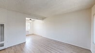 Located at 2232-2240 E Lenita Ln in Santa Ana, CA, this one-bedroom, one-bathroom unit offers a practical and well-organized single-floor layout. The living room is bright and open, featuring light wood-style laminate flooring, crisp white walls, a textured ceiling, and a large sliding window dressed with vertical blinds that invites natural light and outdoor views. An adjacent area connects seamlessly to the kitchen, which is equipped with white cabinetry, granite-style countertops, a double sink, a white range, and a refrigerator. A ceiling fan with a light fixture and windows overlooking the exterior keep the kitchen airy and comfortable, complemented by a wall-mounted air conditioning unit. The bedroom is a well-proportioned private retreat featuring soft carpeting, a window with vertical blinds for natural light, a closet with sliding doors, and access to an additional room or hallway. The bathroom is clean and efficiently designed, featuring a full tub and shower combination with white tile surround, a small privacy window, and wood-style flooring. Throughout the unit, the consistent use of light tones and natural light creates a clean, cohesive ambiance suited for comfortable everyday living.