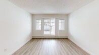 Located in the Ellerslie neighbourhood of southwest Edmonton, this 2-bedroom, 2-bathroom unit offers a practical and well-finished single-floor layout. Light wood laminate flooring runs throughout the main living areas, complemented by textured ceilings and crisp white walls that create a clean, bright atmosphere.

The open-concept living and dining area is generously sized, anchored by a pendant light fixture and vertical blinds that filter natural light. A sliding glass door leads to a private balcony, extending the living space outdoors. The kitchen features warm wood cabinetry, granite-style countertops, a mosaic tile backsplash, and black appliances including a full-size refrigerator, stove, and dishwasher — with frosted glass doors adding a refined touch nearby.

The primary bedroom is a comfortable size with a window overlooking the exterior, while the second bedroom offers similar light and laminate flooring. Both bathrooms are well-appointed with granite-topped vanities and warm wood cabinetry; one includes a walk-in shower with sliding glass doors, and the other a full soaker tub. A dedicated laundry area houses a stacked washer and dryer unit with built-in shelving. Four closets throughout provide excellent storage.