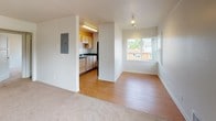 Located at 9061 Seward Park Ave S in Seattle's Seward Park neighborhood, Unit 473 is a single-floor residence designed with practical functionality and a clean, neutral aesthetic throughout. Entry is through a narrow hardwood-floored foyer that leads into the main living area, where soft carpet underfoot and bright white walls create a welcoming atmosphere. A large window allows natural light to fill the space and offers views of the surrounding greenery.

The kitchen is positioned just off the main living area and features light wood cabinetry, dark laminate countertops, a stainless steel sink, and black appliances including a range and refrigerator. An overhead microwave and recessed lighting add to the kitchen's utility. An electrical panel is conveniently accessible from the main living space.

The bedroom is generously proportioned with plush carpeting, white walls, and its own large window that brings in additional natural light. A built-in closet with shelving provides ample storage.

The bathroom includes a full soaking tub with shower, a toilet, and a vanity with light wood cabinetry, all finished in a clean, white palette with tile flooring. A dedicated laundry area with a stacked washer and dryer unit adds exceptional in-unit convenience, rounding out this well-appointed Seattle residence.
