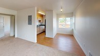 Located at 9061 Seward Park Ave S in Seattle's Seward Park neighborhood, Unit 473 is a single-floor residence designed with practical functionality and a clean, neutral aesthetic throughout. Entry is through a narrow hardwood-floored foyer that leads into the main living area, where soft carpet underfoot and bright white walls create a welcoming atmosphere. A large window allows natural light to fill the space and offers views of the surrounding greenery.

The kitchen is positioned just off the main living area and features light wood cabinetry, dark laminate countertops, a stainless steel sink, and black appliances including a range and refrigerator. An overhead microwave and recessed lighting add to the kitchen's utility. An electrical panel is conveniently accessible from the main living space.

The bedroom is generously proportioned with plush carpeting, white walls, and its own large window that brings in additional natural light. A built-in closet with shelving provides ample storage.

The bathroom includes a full soaking tub with shower, a toilet, and a vanity with light wood cabinetry, all finished in a clean, white palette with tile flooring. A dedicated laundry area with a stacked washer and dryer unit adds exceptional in-unit convenience, rounding out this well-appointed Seattle residence.