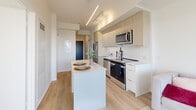 Located on the 9th floor at 610 Martin Grove Road in Toronto's west end, this thoughtfully designed one-bedroom, one-bathroom unit offers a compact yet efficient layout across a single floor. The open-concept kitchen serves as the heart of the space, showcasing light wood cabinetry, stainless steel appliances including a refrigerator, stove, and built-in microwave, a white waterfall island ideal for dining or meal prep, and a subway tile backsplash. Pendant and track lighting adds a modern touch overhead, while light-toned laminate wood flooring runs throughout, creating a warm and cohesive aesthetic. The bedroom is a bright, serene retreat featuring a large double-pane window that frames sweeping views of the surrounding greenery and the Toronto skyline in the distance. A set of sleek sliding closet doors provides ample built-in storage while maintaining the room's clean, minimalist design. The bathroom is finished with large-format porcelain wall tiles in a soft marble-like pattern, complementing the white soaking tub and chrome fixtures for a polished, contemporary feel. The overall ambiance of the unit is modern and airy, with a neutral palette and natural light that make the space feel open and inviting.