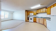 This single-floor unit offers a functional and well-organized layout that flows seamlessly from the entry through to the living and kitchen areas. The kitchen is a standout feature, showcasing warm oak cabinetry spanning both upper and lower sections, dark laminate countertops, and a curved counter layout that maximizes workspace. White appliances — including a refrigerator, electric range, built-in microwave, and dishwasher — provide a complete and cohesive look. Light tile flooring throughout the kitchen and entry area adds a clean, easy-to-maintain surface underfoot. The open-concept design connects the kitchen directly to a generously sized living area, which transitions to soft, neutral carpeting. A large window in the living space invites natural light, creating a bright and airy atmosphere. The bedroom continues the carpeted flooring and features a wide window with blinds, allowing for adjustable light and privacy. The bathroom is equipped with oak vanity cabinetry, a single-basin sink, a wall mirror with overhead lighting, and a full tub-and-shower combination, all set on tile flooring. Textured ceilings are found throughout, adding a subtle design detail consistent across the entire space.