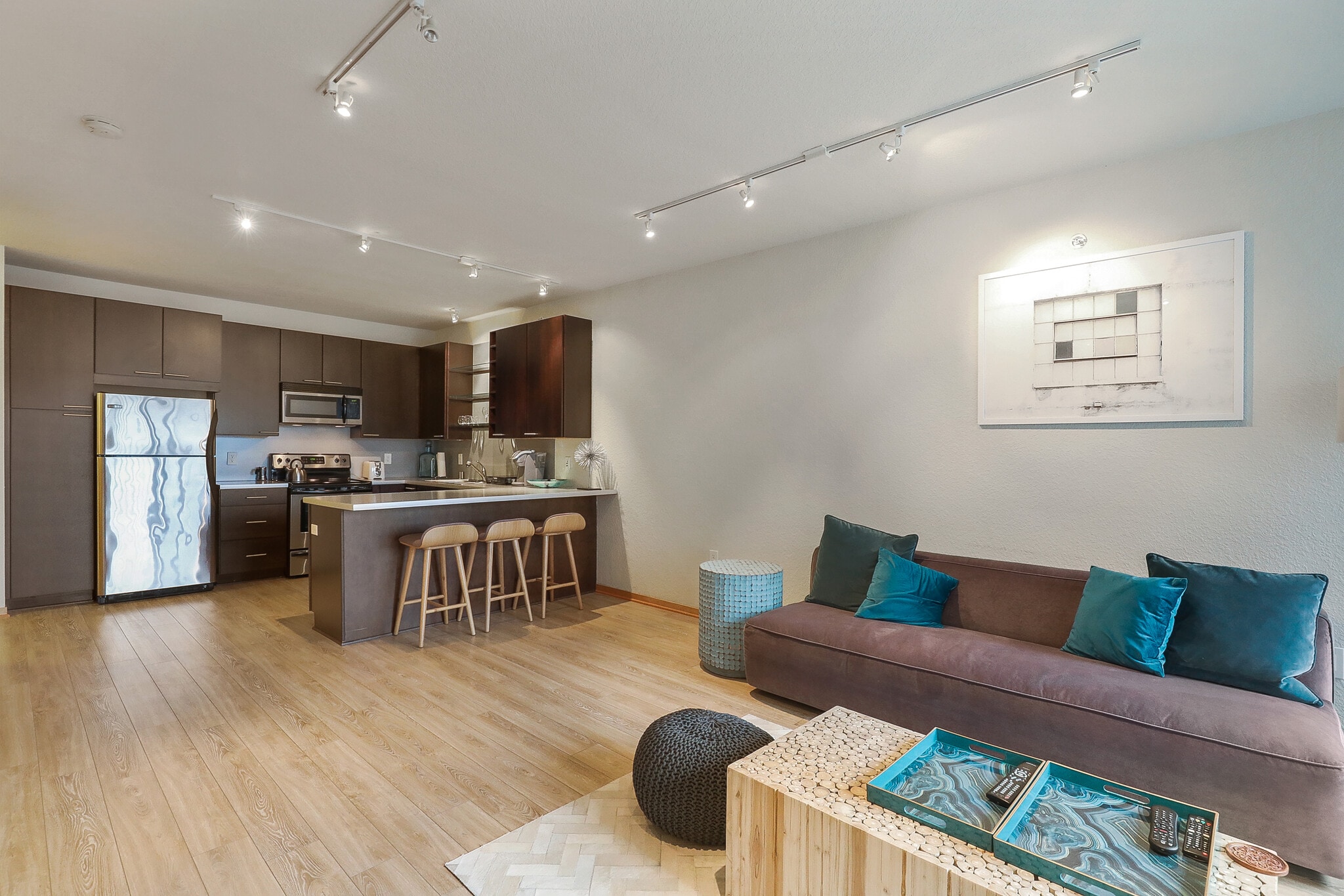Open-concept living room and kitchen area with a modern sofa, coffee table, and kitchen island with bar stools.