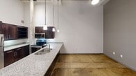 Located in Charlotte's Plaza Midwood neighborhood, this loft-style apartment blends industrial character with modern updates. Soaring ceilings and polished concrete floors set the tone throughout the open living area. Exposed brick accent walls add raw, historic texture that contrasts beautifully with the clean white walls. The kitchen is well-appointed with dark espresso cabinetry, stainless steel appliances, granite countertops, and stylish pendant lighting overhead. The bathroom features a full tub-shower combo with brushed nickel fixtures. Large windows with horizontal blinds allow natural light while framing views of the surrounding greenery.