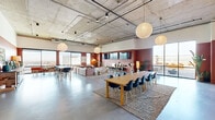 Located at 1000 East Apache Boulevard in Tempe, Arizona, this generously sized amenity lounge spans a single floor and offers a dynamic, open-plan layout designed for both socializing and recreation. The space is defined by its industrial-inspired architecture, featuring exposed concrete ceilings with visible ductwork, polished concrete floors, and bold terracotta and rust-toned accent walls that lend warmth and character throughout.

Large floor-to-ceiling windows and glass doors flood the interior with abundant natural light while framing sweeping views of the Tempe cityscape and surrounding desert landscape. Oversized globe pendant lights complement the high ceilings and contribute to the inviting atmosphere.

The lounge is divided into several distinct functional zones. A generous seating area features large leather sectional sofas arranged to take full advantage of the panoramic window views. A communal dining and work zone offers long wooden tables paired with modern chairs, ideal for group gatherings or collaborative sessions. A dedicated game area includes a foosball table, air hockey table, and billiards table, while a bar-height ledge with stools lines one wall for casual seating. An outdoor terrace, accessible via glass doors, extends the usable space further. The combination of earthy tones, curated greenery, and layered jute rugs creates a cohesive, welcoming ambiance throughout.