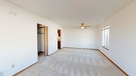 This single-floor residence offers a straightforward, functional layout designed for comfortable everyday living. The main living area is generously proportioned, featuring plush wall-to-wall carpeting, clean white walls with warm wood baseboards, and a ceiling fan that adds both comfort and style. Large windows on multiple sides of the room flood the interior with natural light and provide views of the surrounding neighborhood and open green spaces outside.

The galley-style kitchen is well-equipped with warm oak cabinetry lining both walls, offering ample upper and lower storage. A double-basin sink, electric range, refrigerator, and range hood are all included, and the tile flooring provides a practical, easy-to-clean surface that extends into adjacent areas.

The bedroom is a spacious, carpeted retreat fitted with a ceiling fan and direct access to a walk-in closet. An attached full bathroom features tile flooring, a single-sink vanity with oak cabinetry, a full tub-shower combination, and built-in shelving for convenient storage.

An additional carpeted room serves well as a secondary bedroom or flexible-use space, complete with a window overlooking the yard. The 3D floorplan reveals a cohesive, open arrangement that connects the living, kitchen, and bedroom areas efficiently, making this a practical and well-organized single-level residence.