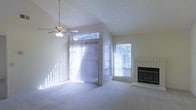This two-story home offers a welcoming and light-filled interior designed for comfortable living. The main living area immediately impresses with its vaulted ceilings, which lend a sense of openness and grandeur to the space. A ceiling fan is centrally positioned, ensuring year-round comfort and complementing the airy feel of the room. Plush wall-to-wall carpeting adds warmth underfoot throughout the living area.

Natural light floods the interior through a combination of large windows, a transom window set high along the vaulted wall, and a full sliding glass door dressed with vertical blinds — offering seamless access to the outdoors while maintaining privacy. The multiple window placements allow light to shift throughout the day, creating a bright and inviting atmosphere at all hours.

A classic brick fireplace anchors one wall of the living room, serving as a charming focal point that adds both character and coziness to the space. The fireplace features a traditional hearth surround and dark metal doors, making it both functional and visually appealing.

The textured ceiling throughout adds a subtle architectural detail consistent with the home's classic styling. Altogether, this two-story residence balances practicality with warmth, offering a comfortable and well-lit environment suited to a variety of lifestyles.