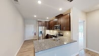 Located at 511 Stallion Circle West in Toms River, New Jersey, this single-floor residence offers a thoughtfully designed layout with contemporary finishes throughout. The open-concept living and dining area features light hardwood-style flooring, recessed lighting, and neutral tones that create a bright, welcoming atmosphere. A sliding glass door leads to a private balcony with outdoor views, bringing additional natural light into the living space.

The kitchen is a standout feature, equipped with rich dark-stained cabinetry, granite countertops, a subway tile backsplash, and a full suite of stainless steel appliances including a gas range, built-in microwave, and French door refrigerator. A peninsula with an undermount sink and additional granite surface space provides both functionality and a natural divide between the kitchen and living area.

The bedrooms are finished with plush carpeting and feature generous windows. The primary bedroom includes access to a walk-in closet with built-in shelving and cabinetry. The primary bathroom offers a glass-enclosed walk-in shower, a dark-framed vanity mirror, and granite-topped vanity. A secondary bathroom mirrors the same refined aesthetic with coordinating tile flooring and dark wood cabinetry.