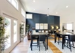 Evergreen at Hickory Valley presents a thoughtfully designed single-floor community space that seamlessly blends modern aesthetics with welcoming functionality. The expansive main area immediately impresses with its soaring vaulted ceilings, which are accentuated by clerestory windows that flood the interior with natural light throughout the day. Warm hardwood flooring extends across the entire space, unifying the various zones and adding a timeless, inviting quality to the overall ambiance.

A dramatic navy accent wall serves as a striking focal point, adding depth and sophistication to the main gathering area. High-top tables and seating arrangements provide flexible spaces for socializing, working, or meeting, while recessed lighting and ceiling fans ensure comfort at any time. Large floor-to-ceiling windows and glass doors along one wall open the space to outdoor views, reinforcing the connection between the interior and the natural surroundings.

Distinct alcoves branch off from the central area, including a dedicated workspace with a striped accent wall and modern standing desks, as well as a cozy lounge corner furnished with comfortable seating. A kitchen area is also visible, supporting the space's community-oriented design. Together, these elements create a dynamic, multi-purpose environment that is both stylish and highly functional.