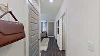 This single-story space is designed with a clean, contemporary aesthetic that balances functionality and style. The entry hallway sets the tone with dark hardwood-style flooring, crisp white walls, and paneled gray doors that carry consistently throughout the unit, creating a cohesive visual flow.

The kitchen is a standout feature, outfitted with white shaker cabinetry, granite countertops, a tile backsplash, and stainless steel appliances including a refrigerator, range, microwave, and dishwasher. A central island with granite countertop and seating for two anchors the space, illuminated by a trio of geometric black pendant lights. The kitchen opens directly into the living area, which benefits from multiple large windows dressed with linen drapes, allowing ample natural light to fill the space.

The two bedrooms are carpeted and well-proportioned, each featuring large windows, ceiling fans, and paneled gray doors. One bedroom features a distinctive horizontally striped accent wall, adding a decorative touch.

The bathroom is finished with dark hardwood-style flooring, a white vanity with black hardware, and a clean, minimalist design. Throughout the space, consistent use of black hardware and neutral tones creates a modern, unified atmosphere.