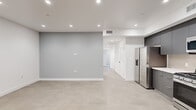 Located at 8940 Reseda Blvd in Northridge, CA, this thoughtfully designed 2-bedroom, 2-bathroom unit offers a clean, modern aesthetic across a single floor. The open living and kitchen area is anchored by a well-appointed kitchen featuring full-height charcoal gray cabinetry, white quartz countertops, a tile backsplash, and a complete suite of stainless steel appliances including a gas range, over-the-range microwave, dishwasher, and French door refrigerator. Recessed lighting illuminates the space throughout, complementing the light-toned tile flooring found across all rooms. The bedrooms offer a calm, neutral palette with soft gray accent walls, natural light from windows with views of greenery, and sliding mirror-panel closet doors with built-in shelving. The primary bedroom includes a sliding glass door opening to a private outdoor area. Both bathrooms are finished in a contemporary style, featuring large-format tile flooring, sleek gray vanities with white countertops, and frameless glass sliding shower doors over soaking tubs. A connecting hallway with a louvered closet door provides convenient access between rooms. The unit's clean lines, modern hardware, and consistent finishes create a cohesive, move-in-ready living environment.
