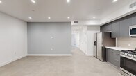 Located at 8940 Reseda Blvd in Northridge, CA, this thoughtfully designed 2-bedroom, 2-bathroom unit offers a clean, modern aesthetic across a single floor. The open living and kitchen area is anchored by a well-appointed kitchen featuring full-height charcoal gray cabinetry, white quartz countertops, a tile backsplash, and a complete suite of stainless steel appliances including a gas range, over-the-range microwave, dishwasher, and French door refrigerator. Recessed lighting illuminates the space throughout, complementing the light-toned tile flooring found across all rooms. The bedrooms offer a calm, neutral palette with soft gray accent walls, natural light from windows with views of greenery, and sliding mirror-panel closet doors with built-in shelving. The primary bedroom includes a sliding glass door opening to a private outdoor area. Both bathrooms are finished in a contemporary style, featuring large-format tile flooring, sleek gray vanities with white countertops, and frameless glass sliding shower doors over soaking tubs. A connecting hallway with a louvered closet door provides convenient access between rooms. The unit's clean lines, modern hardware, and consistent finishes create a cohesive, move-in-ready living environment.