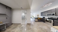 This thoughtfully designed one-bedroom, one-bathroom unit offers a seamless blend of modern aesthetics and functional living across a single floor. Gleaming polished marble-look floors flow throughout the main living areas, immediately establishing a sophisticated tone.

The open-concept kitchen and living room form the heart of the space. The kitchen is outfitted with dark grey shaker-style cabinetry with brushed gold hardware, dark granite countertops, stainless steel appliances, and a striking copper farmhouse sink. A breakfast bar with seating provides a casual dining option. A geometric LED ceiling fixture adds a contemporary touch overhead.

The living area is bright and airy, featuring crisp white walls and access to a private balcony through a full-length glass door framed in matte black. A bold dark slatted accent wall anchors the living room, adding depth and contrast to the otherwise light palette. Large windows with layered roller shades allow for versatile light control.

The bedroom is a calm retreat, offering balcony access through a sliding glass door, generous closet space with clean-lined bifold doors, and the same refined flooring.

The bathroom is clean and modern, showcasing a large frameless glass walk-in shower with white subway tile and a rainfall showerhead, a marble-top vanity, and crisp white tile floors.