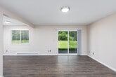 This single-floor space offers a practical and comfortable layout with thoughtfully appointed rooms throughout. The living area is a standout feature, finished with durable wood-look flooring and neutral beige walls that create a clean, versatile backdrop. A sliding glass door floods the space with natural light and opens to a view of a lush green lawn and surrounding trees, providing a pleasant outdoor connection. A side window and baseboard heating add to the room's functionality.

Adjacent to the living area, the galley-style kitchen is efficiently designed with ample white shaker cabinetry, dark countertops, and a stainless steel sink. Appliances include an electric range, stainless steel refrigerator, and over-the-range microwave. Track lighting illuminates the workspace, and light wood-look flooring ties the space to the rest of the unit.

The bedrooms are carpeted for comfort, each featuring neutral tones, natural window light, and baseboard heating. One bedroom includes a sliding closet door with an organized interior rod system. The bathroom is equipped with a full-size soaking tub and shower combo with chrome fixtures and clean white surround panels, complemented by warm beige walls.