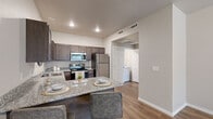 Located at 3911 N Old Missouri Rd in Fayetteville, Arkansas, this single-story, four-bedroom, two-bathroom unit offers a practical and well-appointed layout. The combined kitchen and living area serves as the heart of the home, featuring dark wood cabinetry, granite-style countertops, a full suite of stainless steel appliances — including a refrigerator, electric range, microwave, and dishwasher — and a breakfast bar with seating. Wood-look plank flooring runs through the kitchen, living area, and select bedrooms, lending a cohesive, modern aesthetic throughout. The four bedrooms are comfortably sized, each equipped with a ceiling fan and natural light from windows with blinds. Flooring varies between wood-look planks and plush carpet depending on the room. The hallway connects the bedrooms to two full bathrooms, both finished with dark wood vanities, granite-style countertops, and tub-shower combinations with sliding glass doors. A dedicated laundry area provides added convenience, and a closet offers supplemental storage. Neutral wall tones and consistent trim work create a clean, uniform look throughout the entire unit.